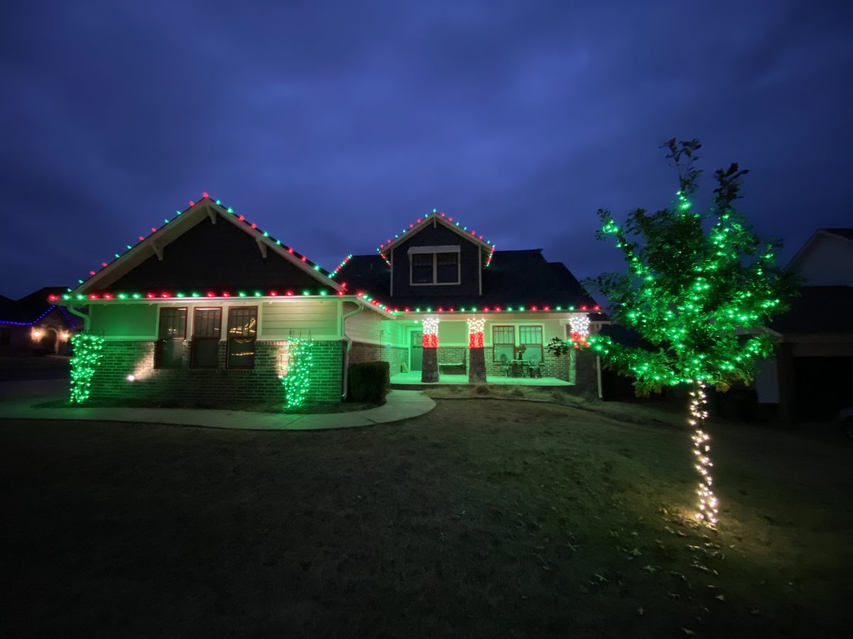 Craftsman home in Edmond outlined in red and green Christmas lights with a lit tree in the front yard