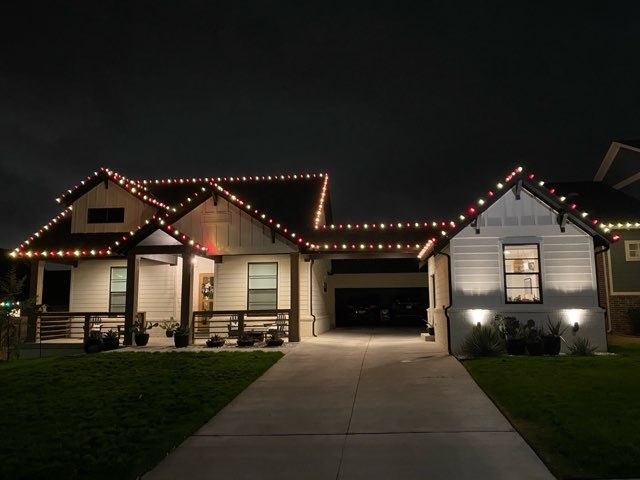 Two story home outlined in warm white lights along the roofline and garage