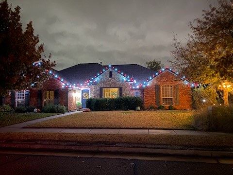Ranch home lined in multicolor Christmas lights along the roof and porch