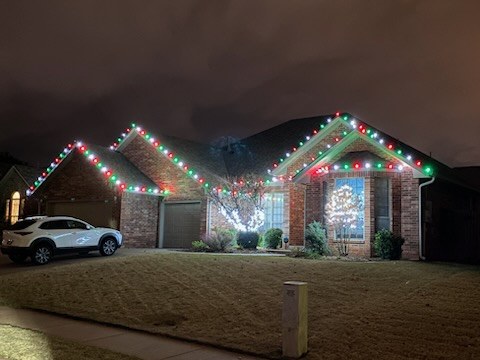 Brick home outlined in red and green lights with a lit wreath on the gable