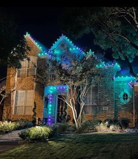 Home lit in teal and green across the roofline, trees and landscaping