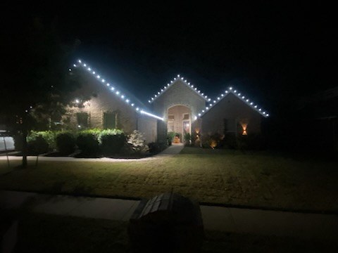 Peaked roofline outlined in cool white lights above a dark lawn