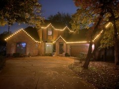 Home lit along the roofline with the surrounding trees wrapped in lights