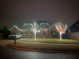 Front yard with wrapped trees and a fully lit roofline behind them
