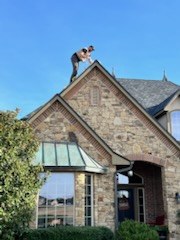 Installer on the roof of a stone home running a light line