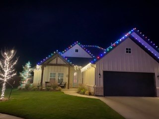 Home in multicolor roofline lights with two wrapped trees in the yard