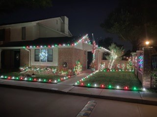 Brick home in red and green roofline lights with a lit tree beside it